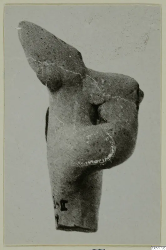 Terracotta figurine fragment of a torso with one arm bent across the chest, head missing, against a plain background.