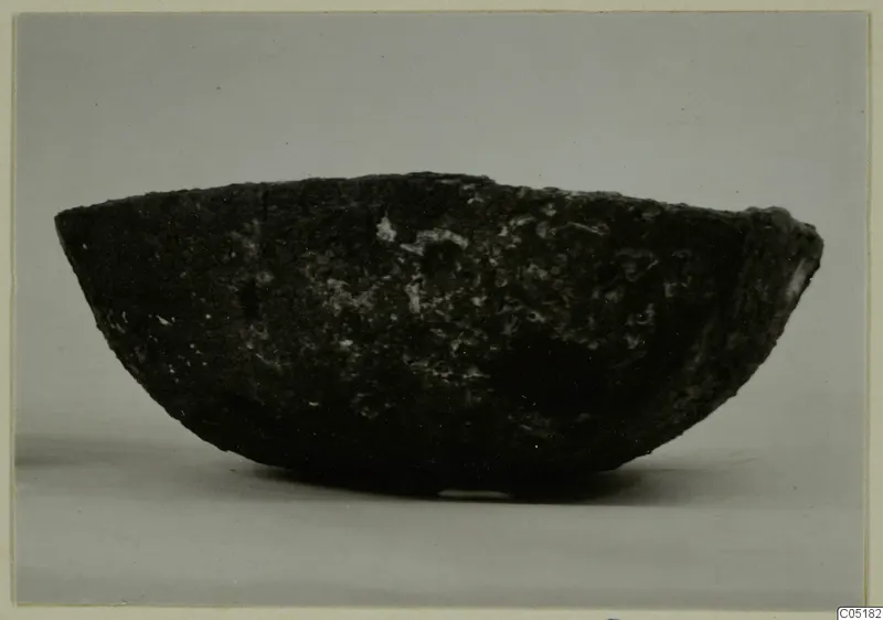 Dark, rough-surfaced bowl seen from the side against a grey backdrop
