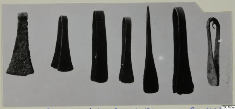 Seven bronze objects from Lapithos Tomb 320 laid in a row on a pale grey background