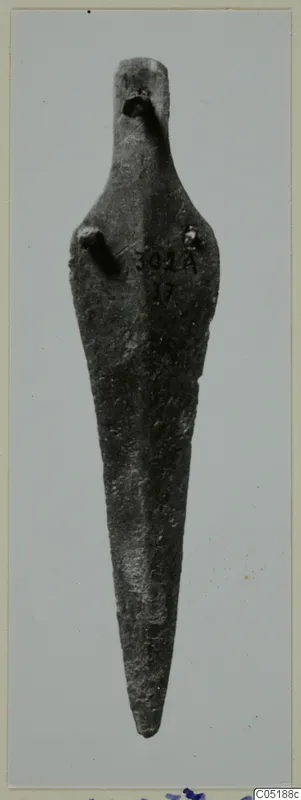 Long pointed bronze object from Lapithos Tomb 302A, tapering to a point, shown against a grey card.