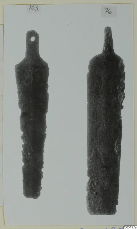 Two bronze tools with long tapering blades and narrow tangs, photographed on a mounted card.