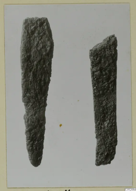 Two corroded metal objects from Lapithos Tomb 409, one long and tapering to a point, the other a short flat bar