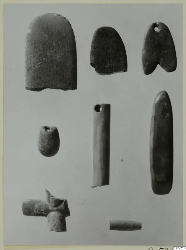 Several small stone objects from Kythrea, including perforated pendants and a tube-shaped piece, on a plain background.