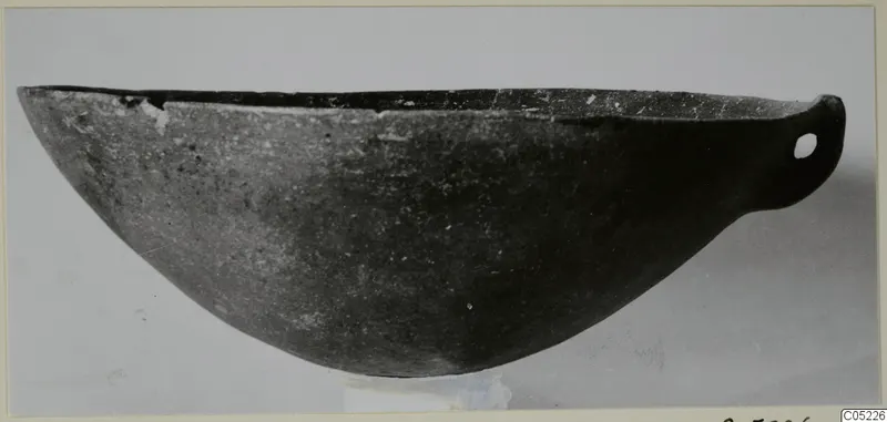 Pottery Black Slip Ware bowl with a small pierced handle at one end, shown in side view