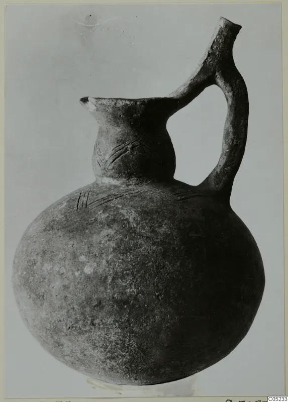 Round-bodied pottery jug with a strap handle and incised lines on neck and shoulder, dark surface