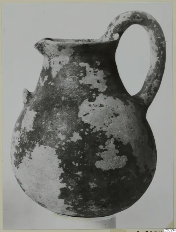 Black Slip Ware jug with a loop handle and a small spout, its dark surface flaking to lighter patches