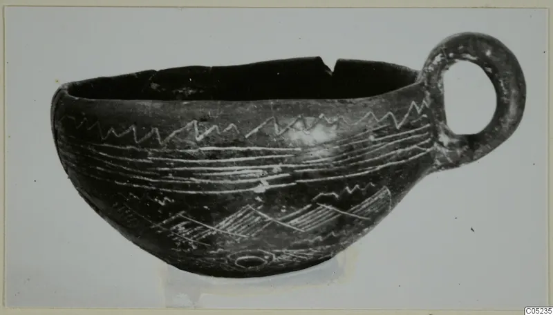 Black polished cup with a large loop handle and pale incised zigzag and banded decoration