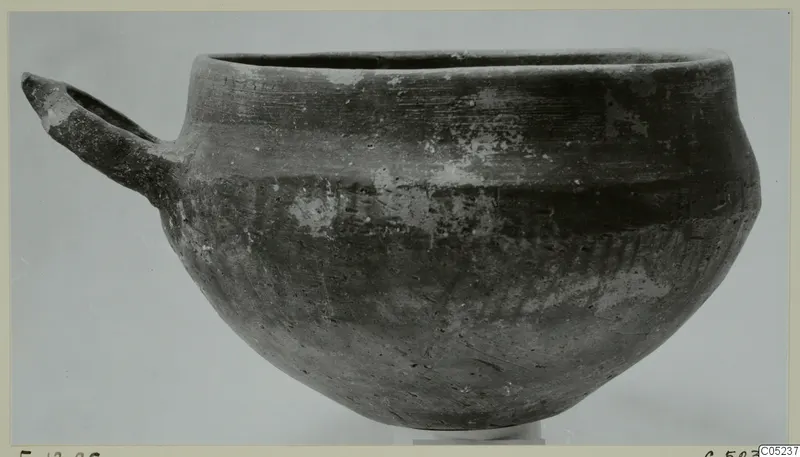 Pottery Monochrome Ware bowl with a single loop handle, photographed from the side against a plain grey background