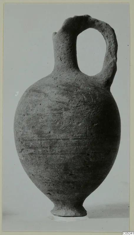 Pottery jug with a single loop handle, Black Lustrous Ware, shown upright against a plain grey background.