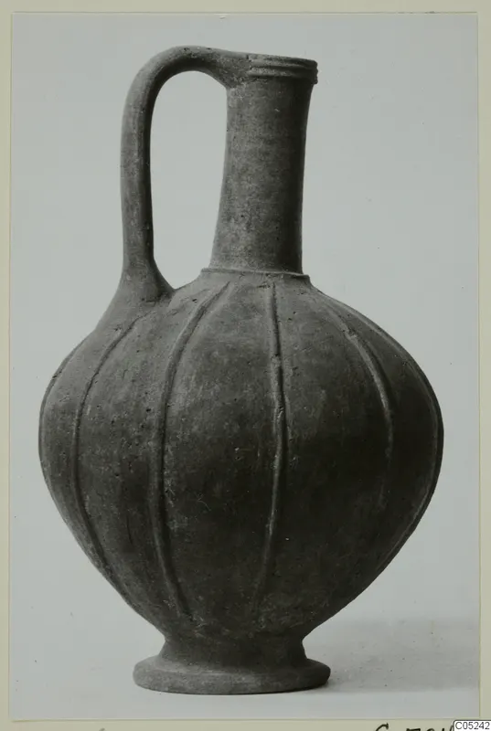 Jug with a single loop handle, a tall neck and a fluted, rounded body on a footed base.