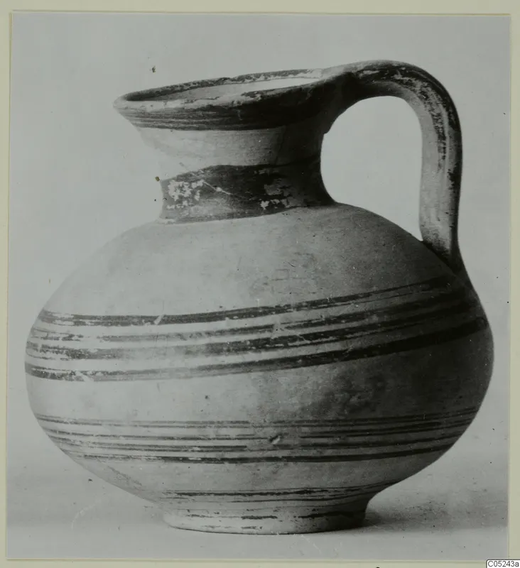 Pottery bowl-jar with a strap handle, a flaring rim and dark painted horizontal bands, shown against a plain background.
