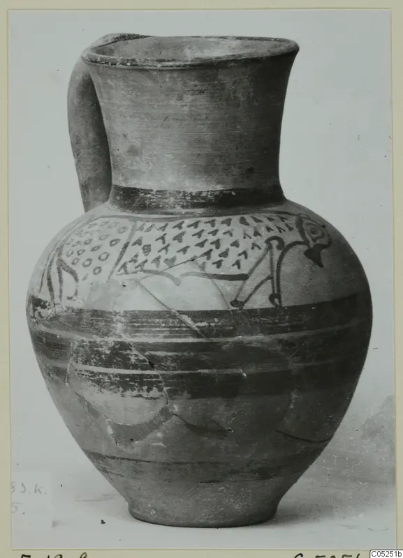 Pottery bowl-jar with a single strap handle and painted triangles, dots and bands, photographed against a pale background