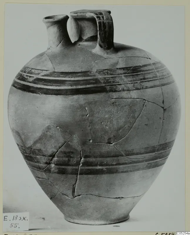 Pottery bowl-jar with a narrow spout, a strap handle and dark painted bands, its surface cracked where fragments have been joined