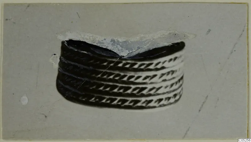 Banded metal object with diagonal chevron pattern, shown centred on a grey card, from Enkomi