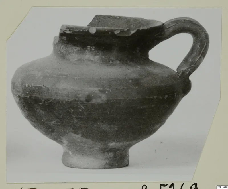 Cypro-Hell.I. jug with a strap handle and a broken rim, shown in side view.
