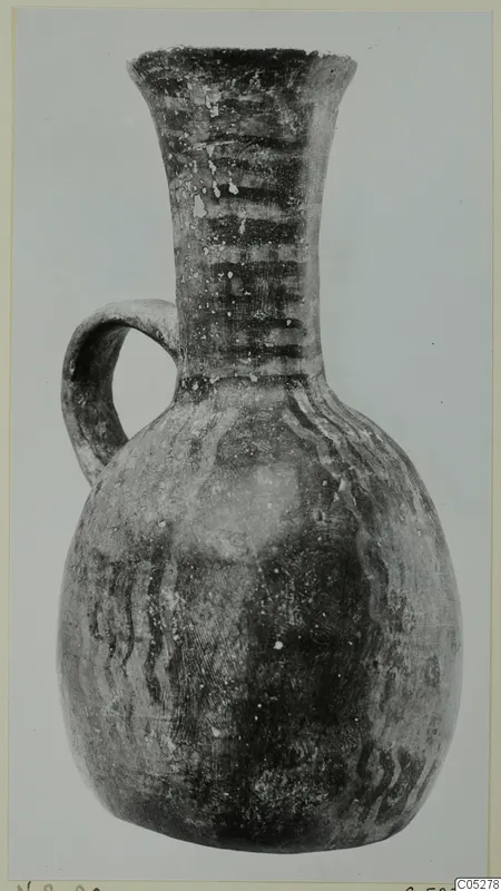 Pottery jug with a single loop handle, flaring neck and dark painted bands, photographed against a plain grey background