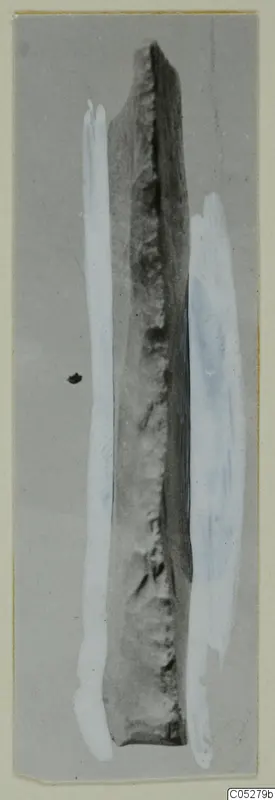 Long narrow stone find from Kythrea, tapering at the top, with a rough dark edge, photographed on a grey background.