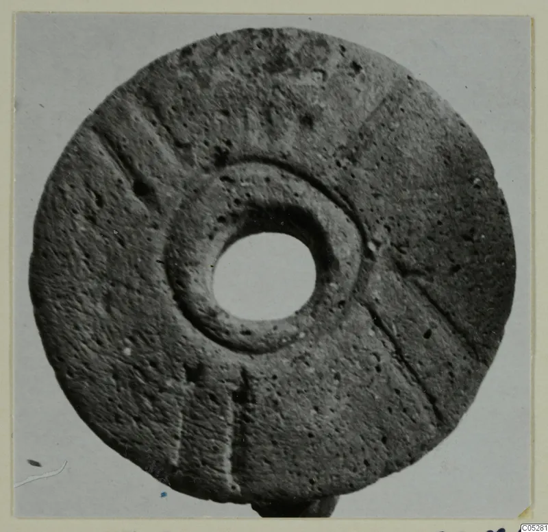 Disc-shaped find with a central hole and incised radial lines, from Lapithos, shown on a pale card mount