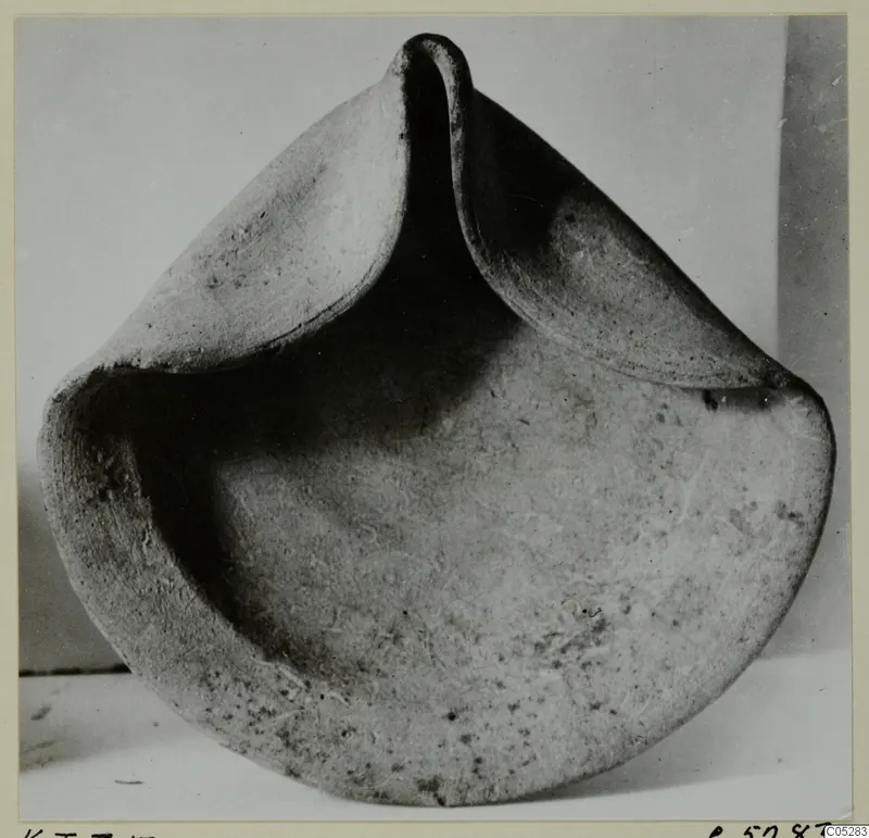 Terracotta bowl-shaped object with a pinched rim rising into three raised lobes, photographed on a light surface.