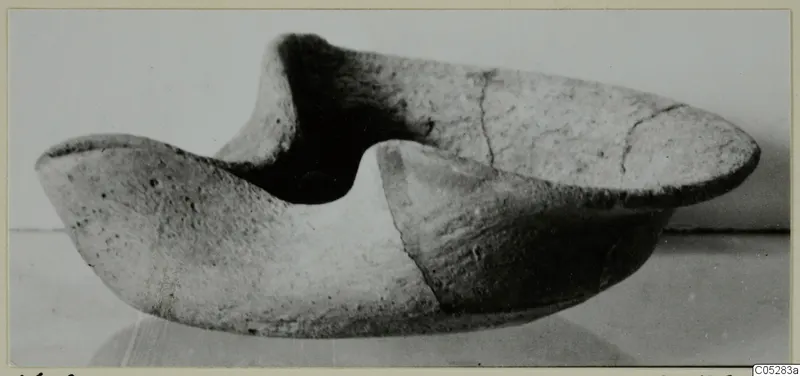 Terracotta lamp in side view, with two raised pinched ends and cracks across the body