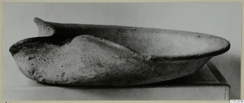 Terracotta lamp with a pinched nozzle, photographed from the side on a flat surface