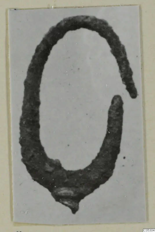 Corroded metal open-ended loop, likely a bronze piece of jewellery, from Arsos, photographed on a grey card.