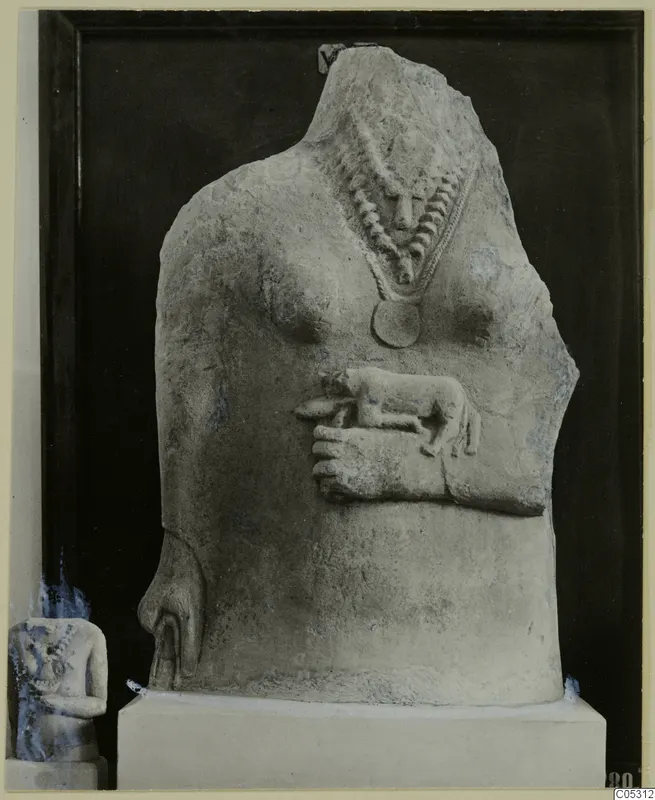 Headless limestone statue torso with a beaded necklace, a disc pendant, and a small carved animal in relief across the belly.