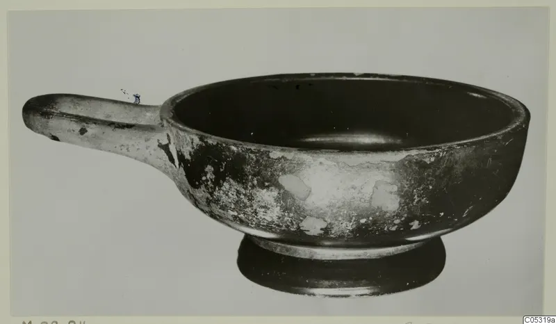 Black glazed bowl with a long horizontal handle and a low ring foot, from Marion