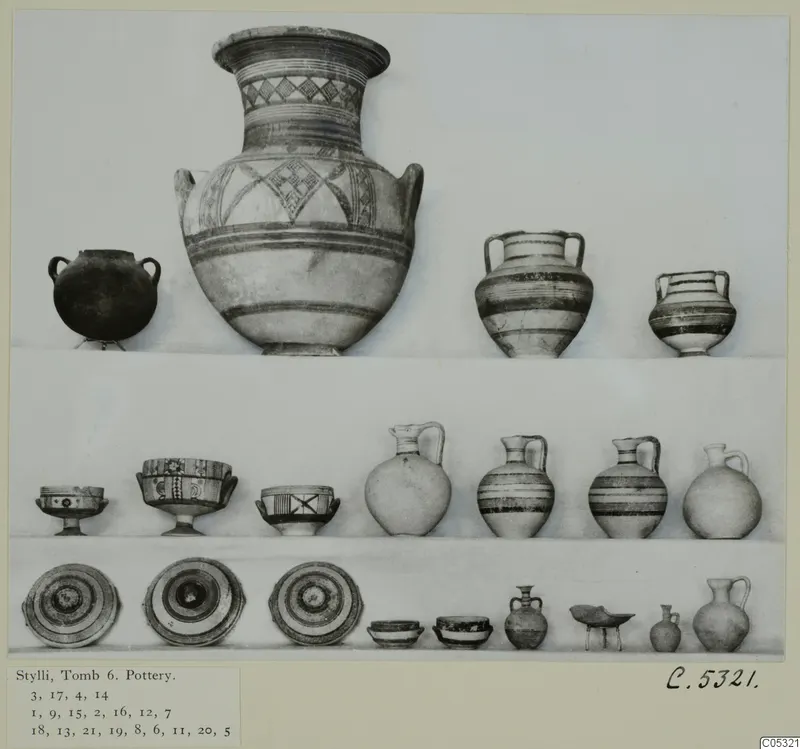 Pottery vessels from Stylli, Tomb 6, arranged in three rows: two-handled jars, jugs, footed bowls and shallow dishes.