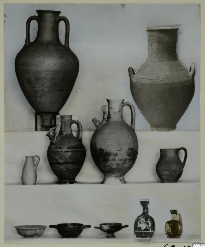 Pottery from Marion, Tomb 18: two large jars, several jugs and small bowls set out on shelves against a plain backdrop