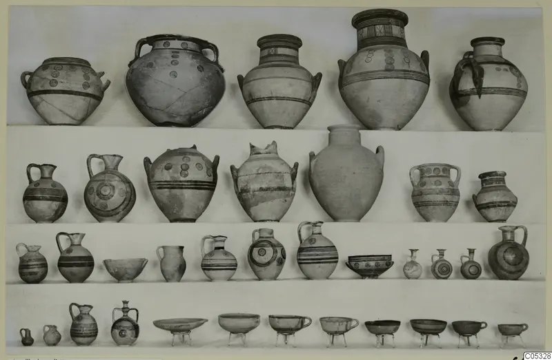 Four rows of painted pottery jars, jugs and bowls displayed on shelves, from Marion Tomb 10