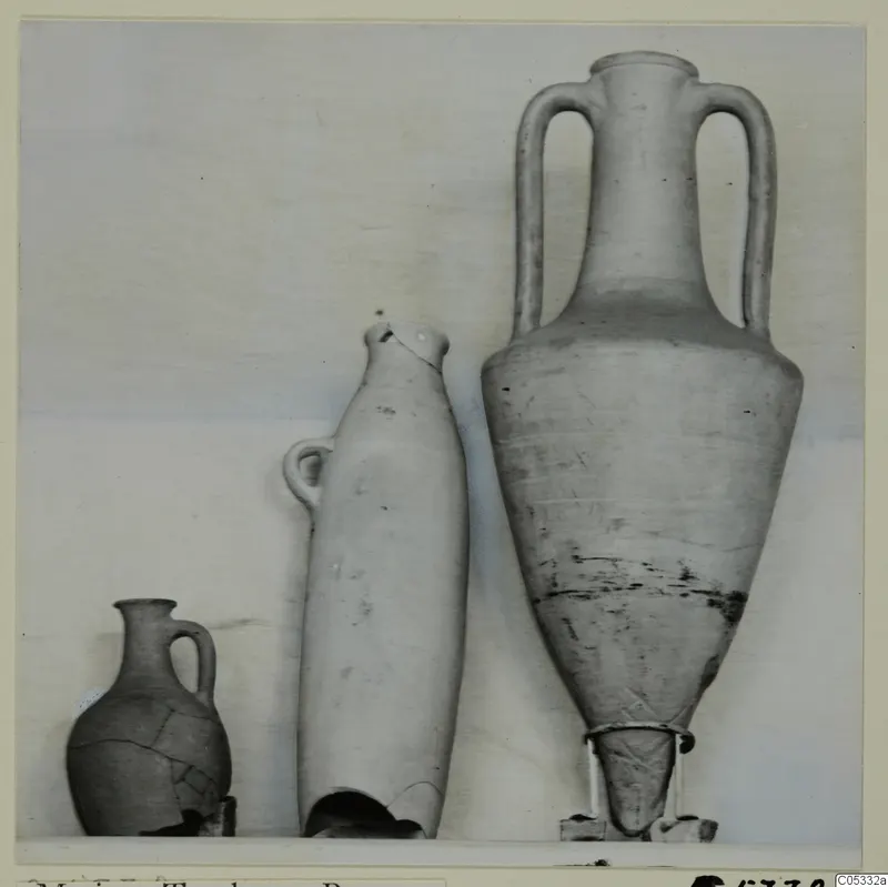 Three pottery vessels on a shelf: a small one-handled jug, a tall narrow vessel with a broken base, and a large two-handled amphora.