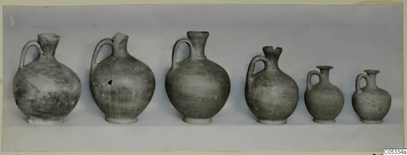 Six small pottery jugs with single handles, in a row from large to small, from Marion Tomb 48.