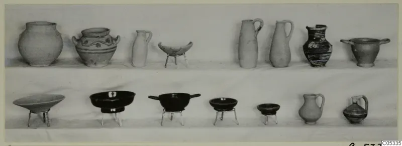 Two rows of pottery jugs and bowls from Marion Tomb 57, set out on a pale surface.