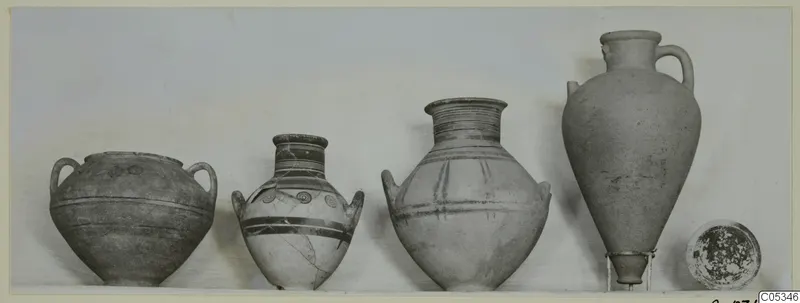 Four pottery vessels and a small dish from Tomb 94 at Marion, standing in a row on a pale surface
