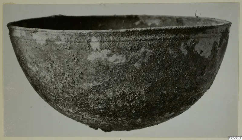 Corroded metal bowl from Marion, Tomb 22, seen from the side against a pale background.