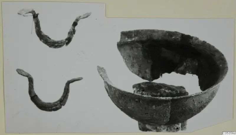 Broken bowl with part of its rim missing, beside two curved corroded metal pieces, on a mounted photograph.