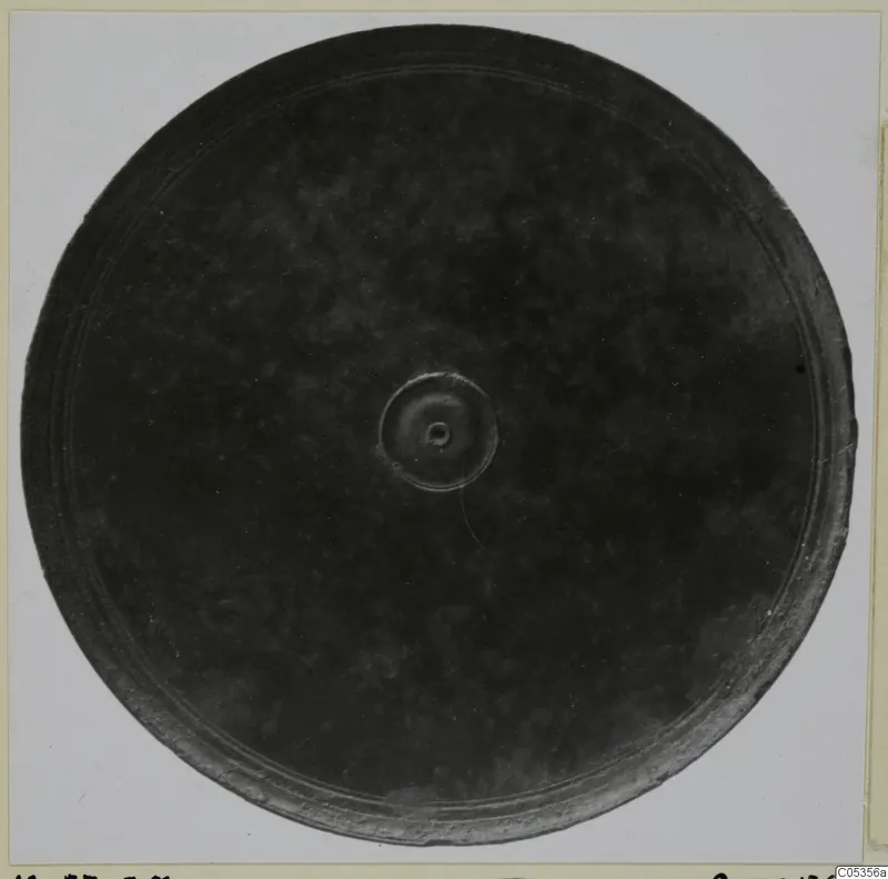 Bronze mirror with a raised central boss and concentric rings near the rim, seen face-on on a pale ground