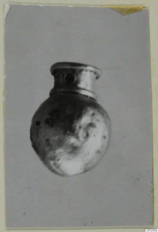 Small rounded metal object with a flared neck and a hole through the side, shown in a single photograph