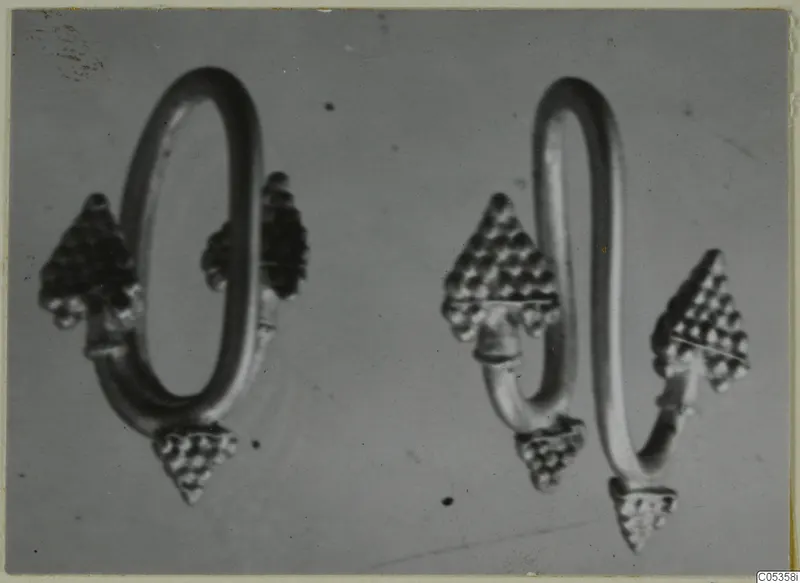 Two gold loop-shaped objects with triangular granulated terminals, photographed on a grey background.
