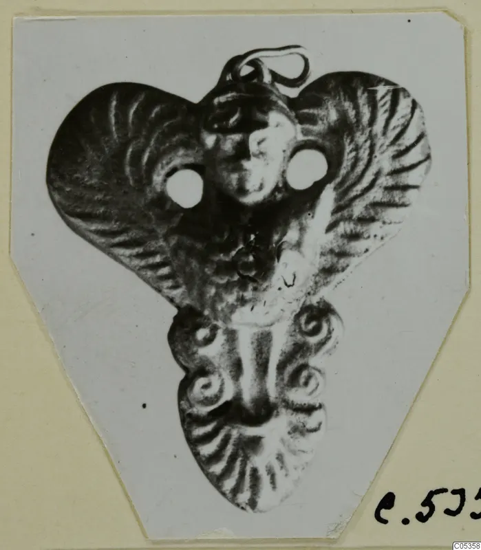 Metal pendant with a small face in relief, two round holes and a loop at the top, from Marion