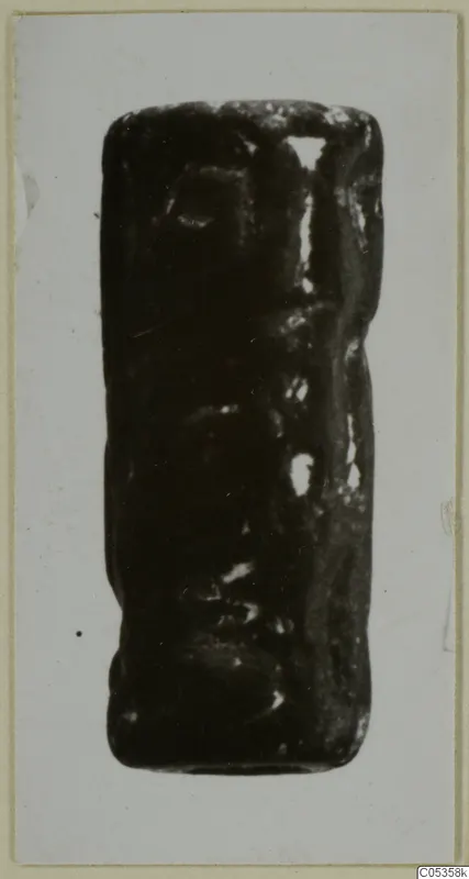 Cylinder seal from Vouni, dark stone with carved surface, photographed upright on a card mount