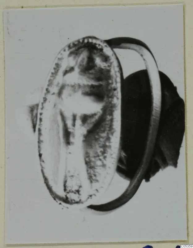 Ring with an oval bezel and a central engraved design, shown large on a card mount.
