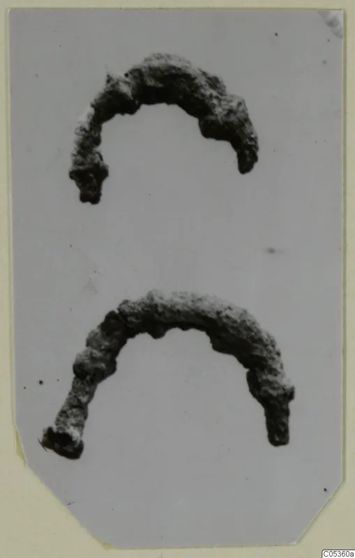 Two corroded bronze arc-shaped personal adornments from Amathus, one above the other.