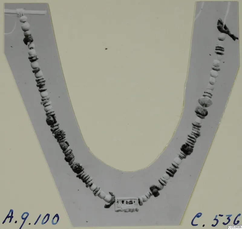 Necklace of pale and dark beads laid in a curve on a grey U-shaped card