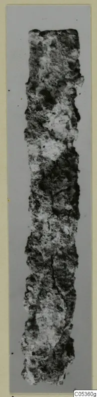Corroded iron knife blade, shown upright, with a rough crusted surface and broken ends.