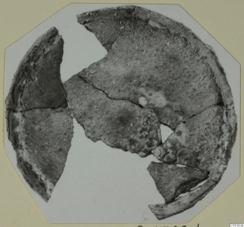 Broken pieces of a round, dark, corroded object from Amathus, shown on a card mount
