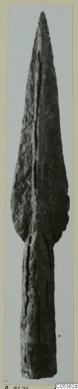 Bronze spearhead from Amathus, a long leaf-shaped blade with a central ridge, shown upright on a mounted print.