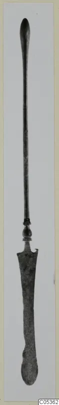 Bronze toilet implement: a long slender rod with a knob and a flat, widened blade end, shown upright.