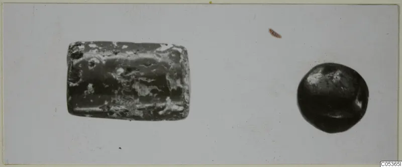 Two stone objects on a pale background: a greenish, mottled cylinder-like object and a smaller dark rounded object